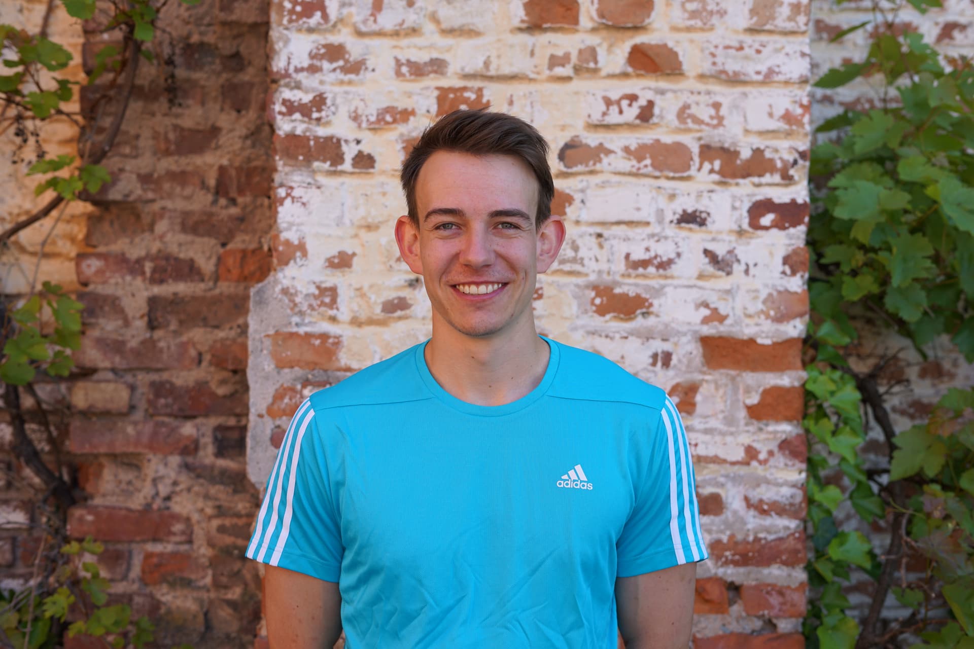Fitness Trainer Sebastian Kirchmann steht vor einer Wand und lächelt in die Kamera