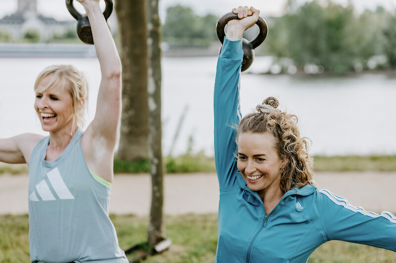 irkeltraining Outdoor: Zwei Frauen trainieren mit Kettlebells am Wasser.