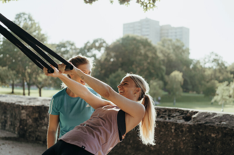 Zirkeltraining Outdoor: Teilnehmerin trainiert mit Schlingenband unter Anleitung.