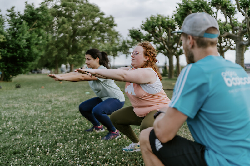 Neujahr Fitness: Funktionelles Gruppentraining im Park mit Kniebeugen, angeleitet von einem Trainer – gemeinsames Outdoor-Workout für Kraft, Stabilität und Motivation.