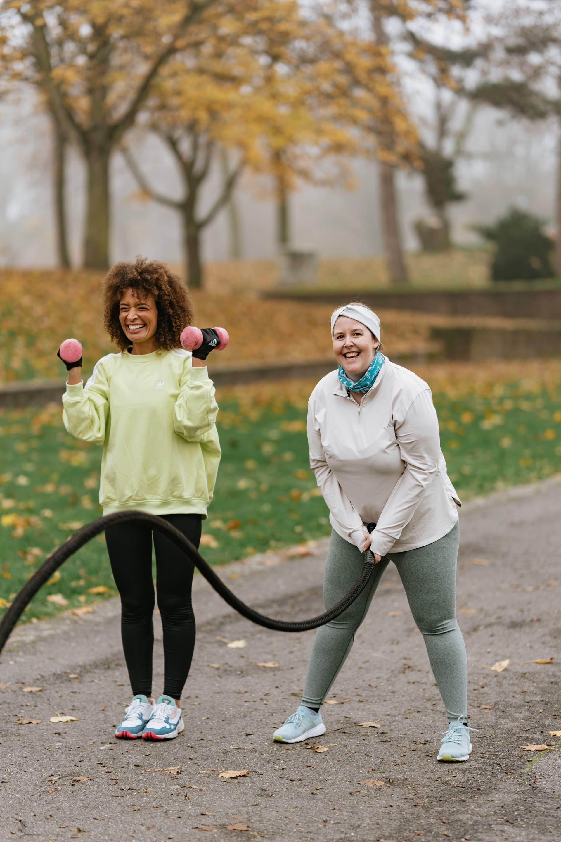 Zwei Frauen trainieren im herbstlichen Park mit Battlerope und Hantel