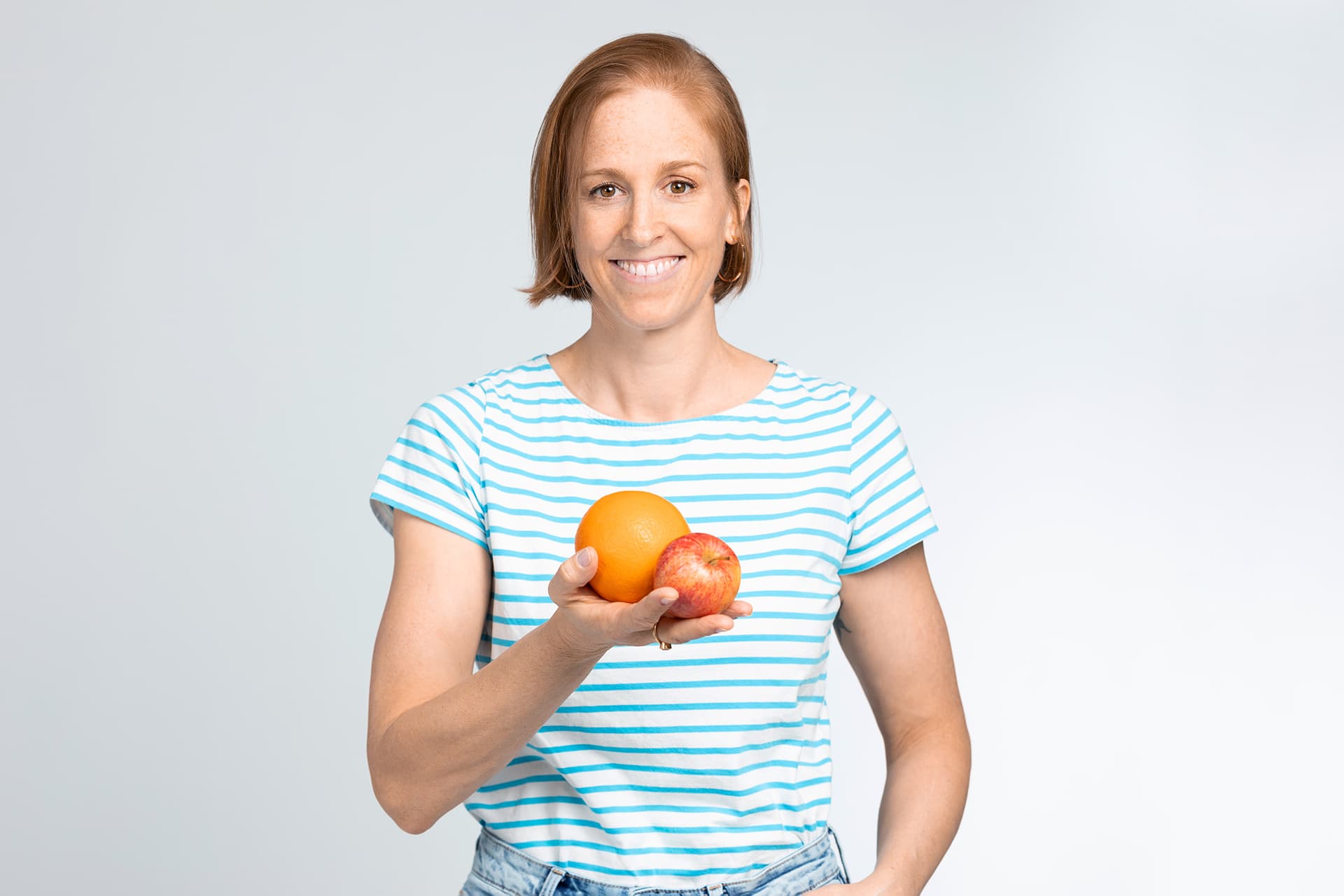 Sarah Viethen trägt ein gestreiftes Shirt und hält Obst in die Kamera